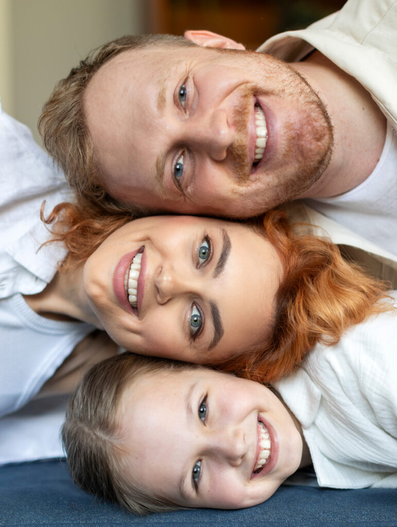 Three people, two adults and one child, lying close together and smiling at the camera.